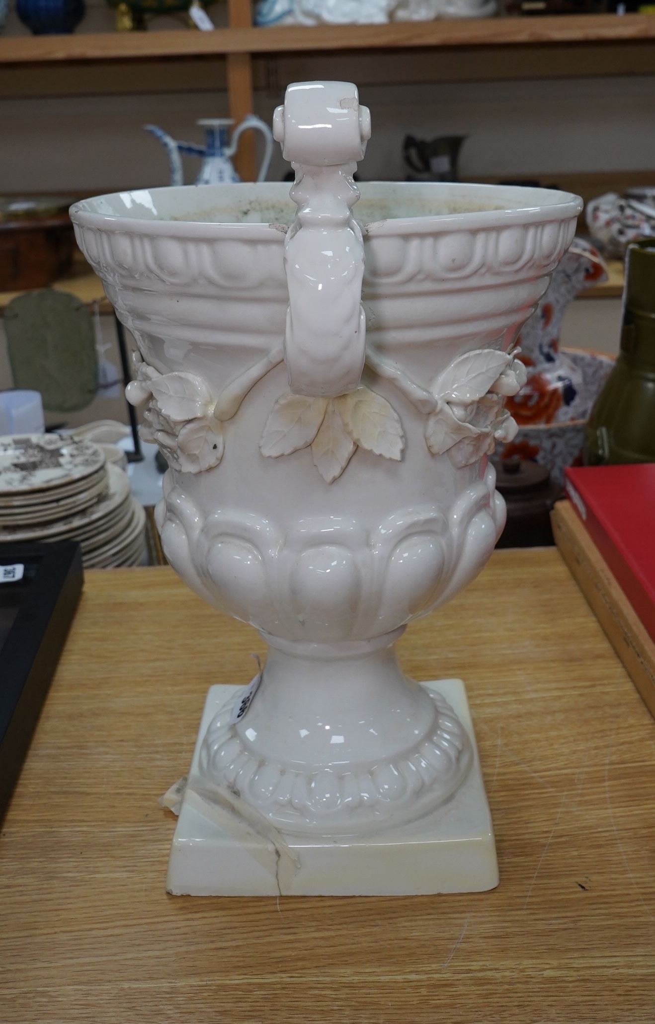 A large cream glazed pottery pedestal vase, with decorative swag of fruit and leaves, 43cm high. Condition - corner of square base broken, glazing chipped on top rim and fruit and leaf decoration broken